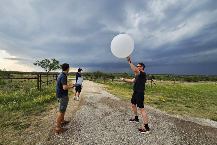 Personen lassen einen Wetterballon vor stürmischem Himmel steigen.